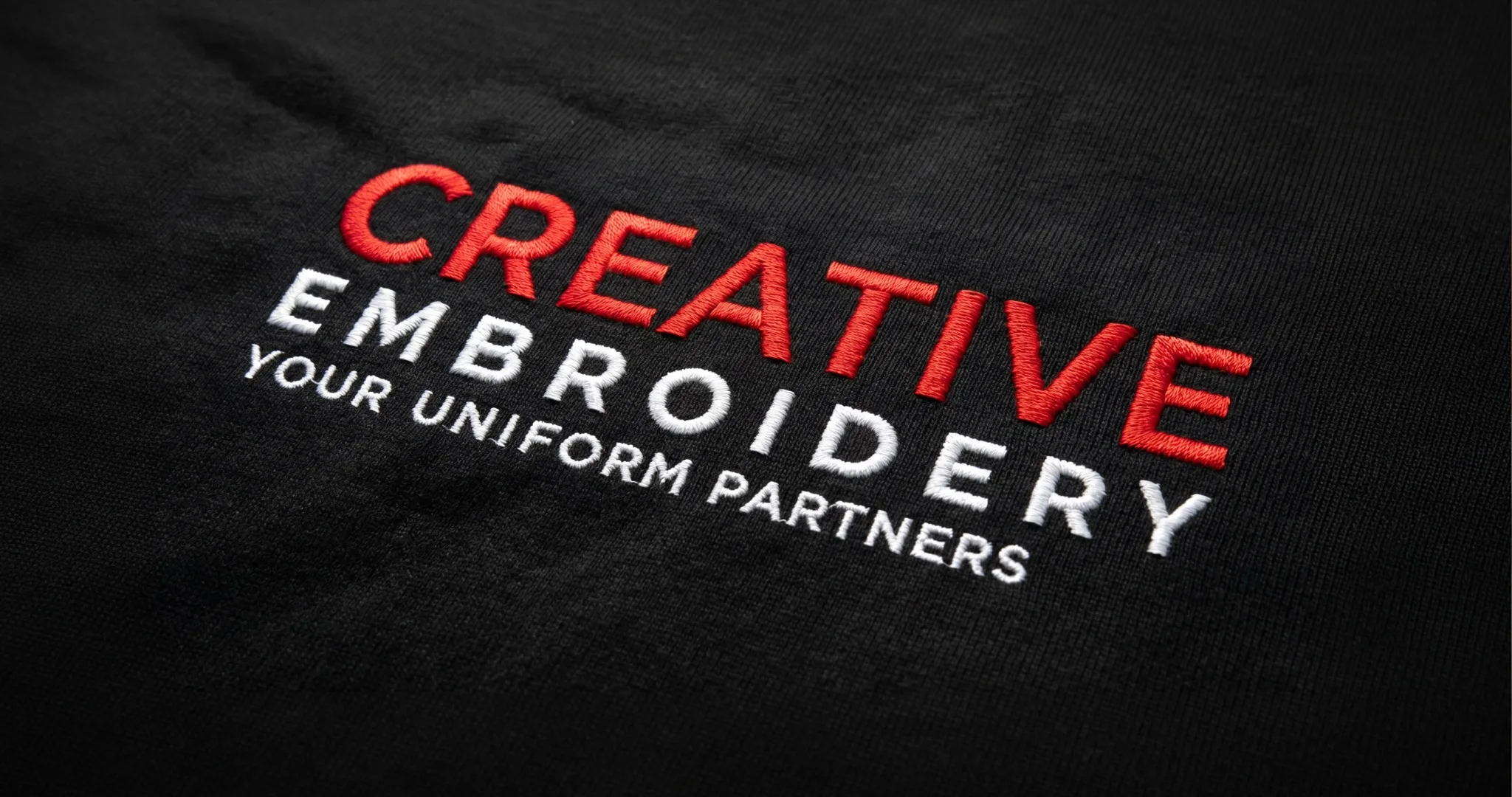 Close-up of the Creative Embroidery logo embroidered on black fabric